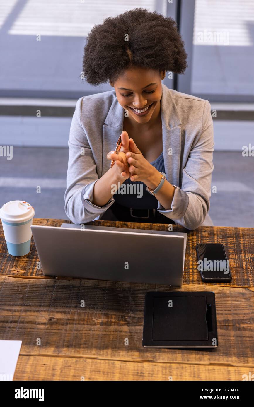 African American woman in business attire sitting at office smiling at laptop with coffee tablet Stock Photo