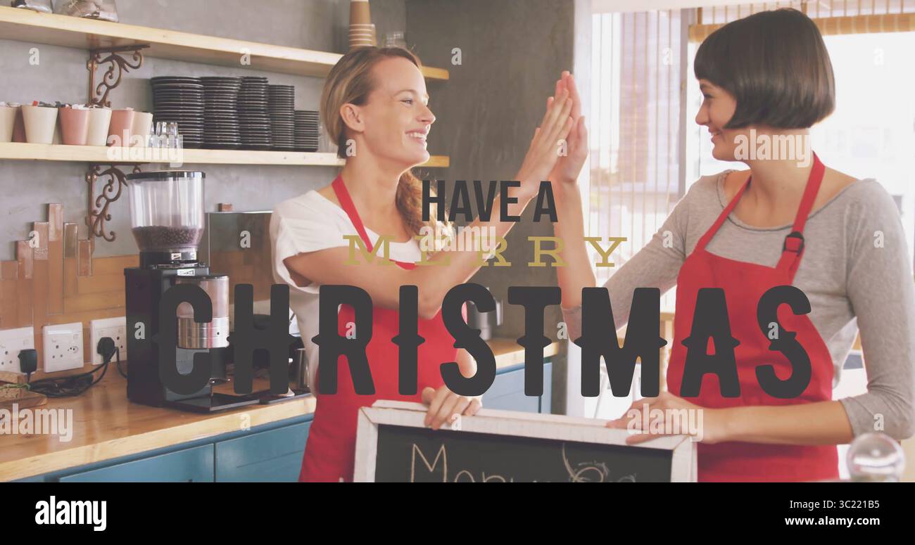High-fiving two baristas in red aprons behind coffee counter, espresso machine and chalkboard sign Stock Photo