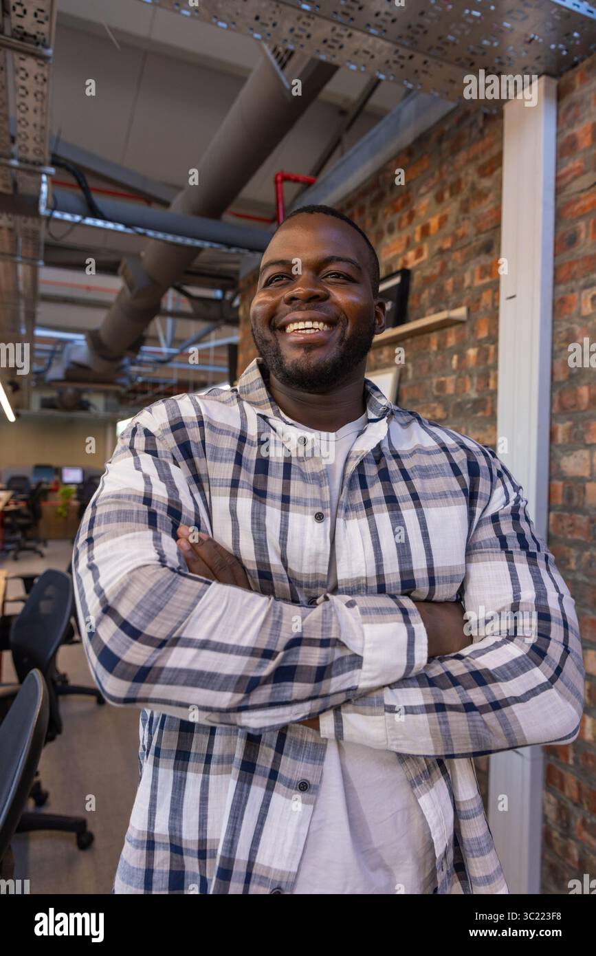 African American man standing with arms crossed and smiling in office with black chairs, ductwork Stock Photo