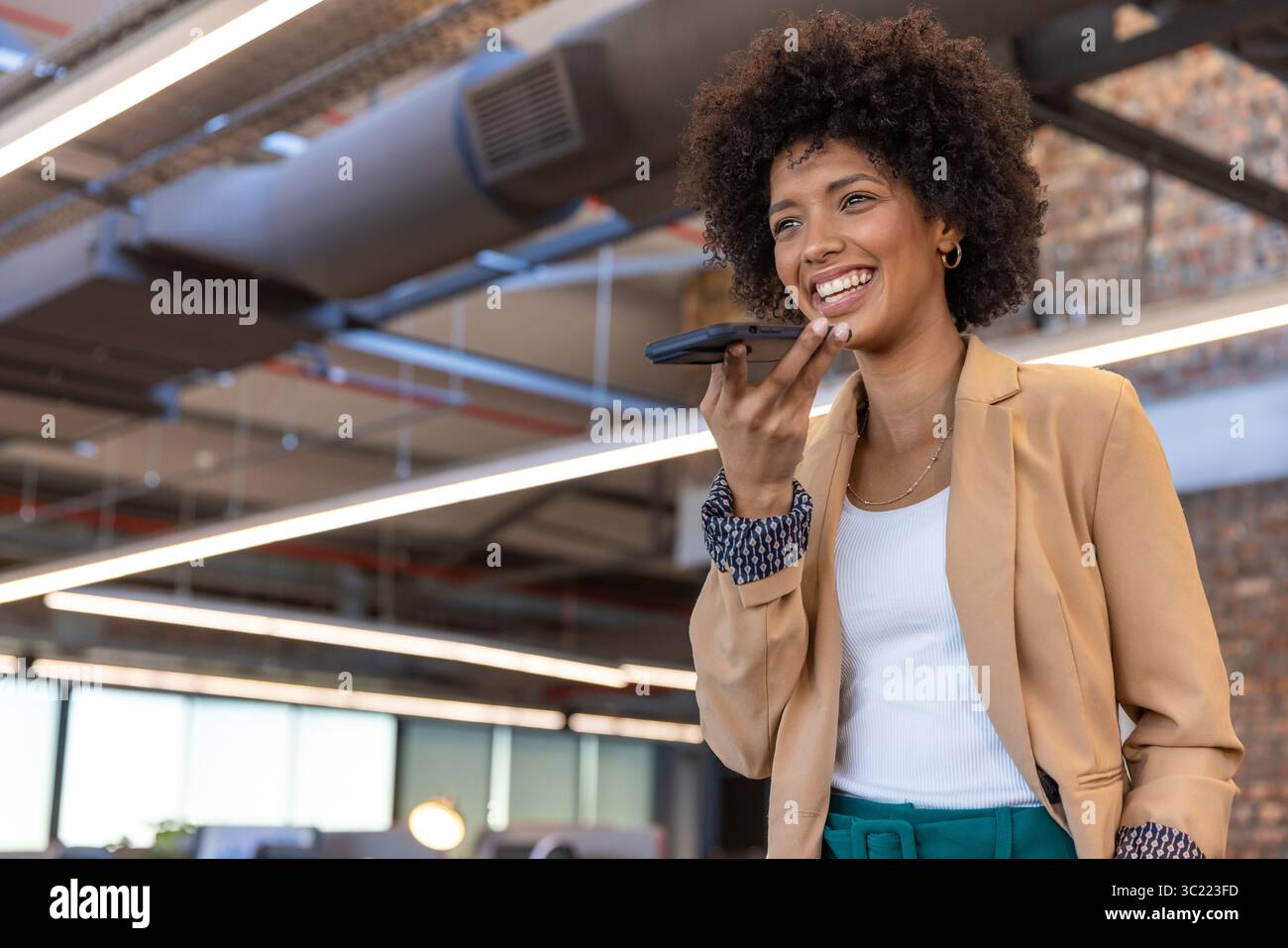 African American woman wearing blazer speaking into smartphone standing in office, copy space Stock Photo