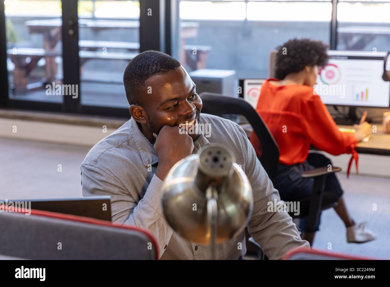 Diverse coworkers wearing business attire working at office desks with metal lamp and dual monitors Stock Photo