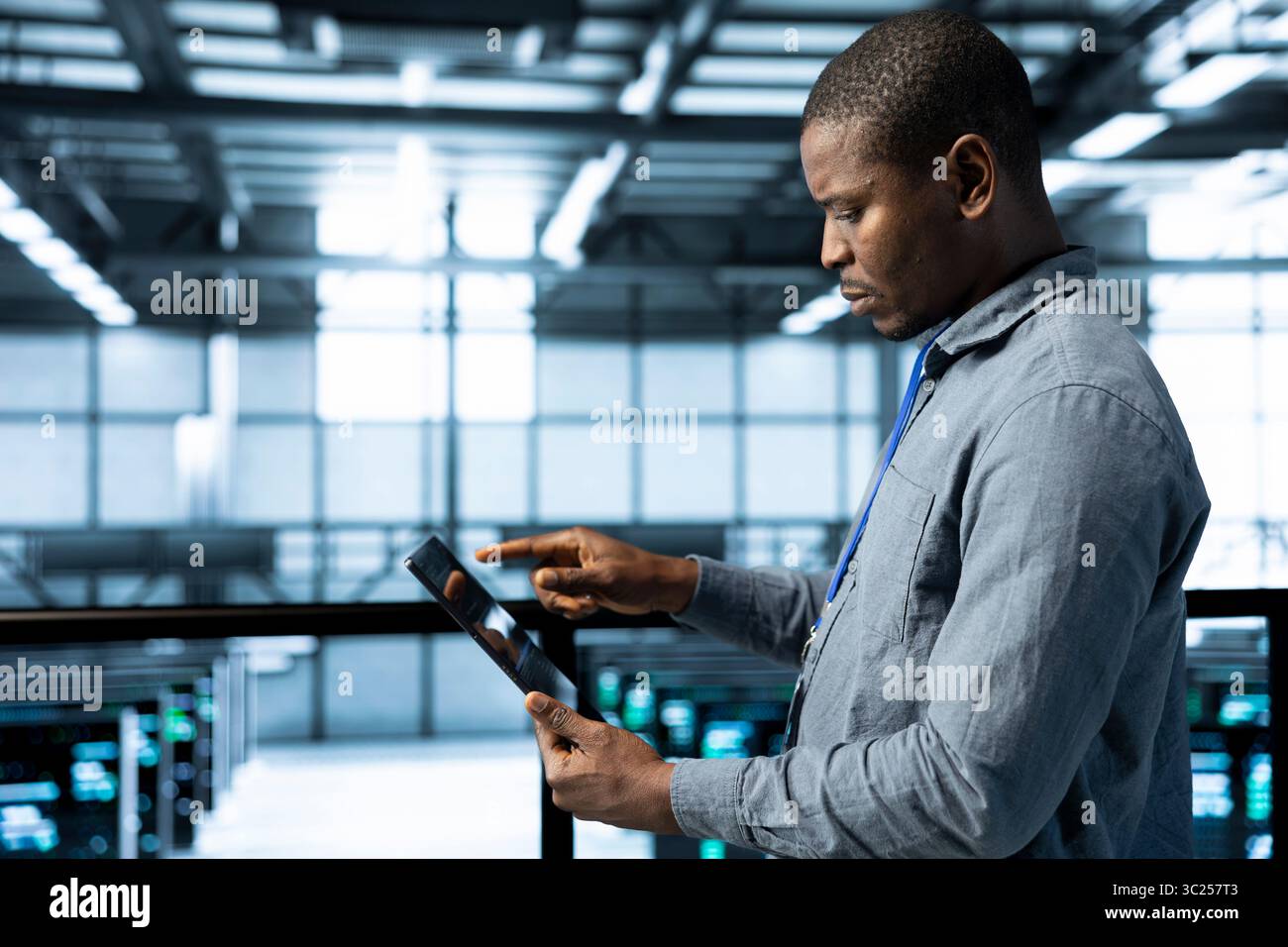Admin in data center using tablet to deploy new server architectures, configuring network virtualization. Man in server room updating storage arrays, verifying settings to maintain stable performance Stock Photo