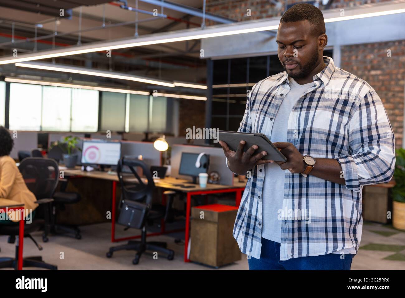African American man standing in office holding tablet with monitors and coffee cup, copy space Stock Photo