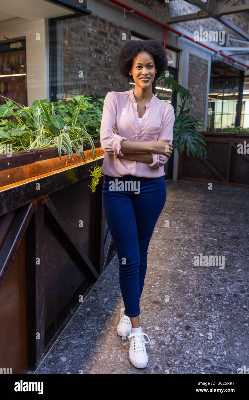 African American woman wearing light pink blouse standing beside wooden planter box in office lobby Stock Photo