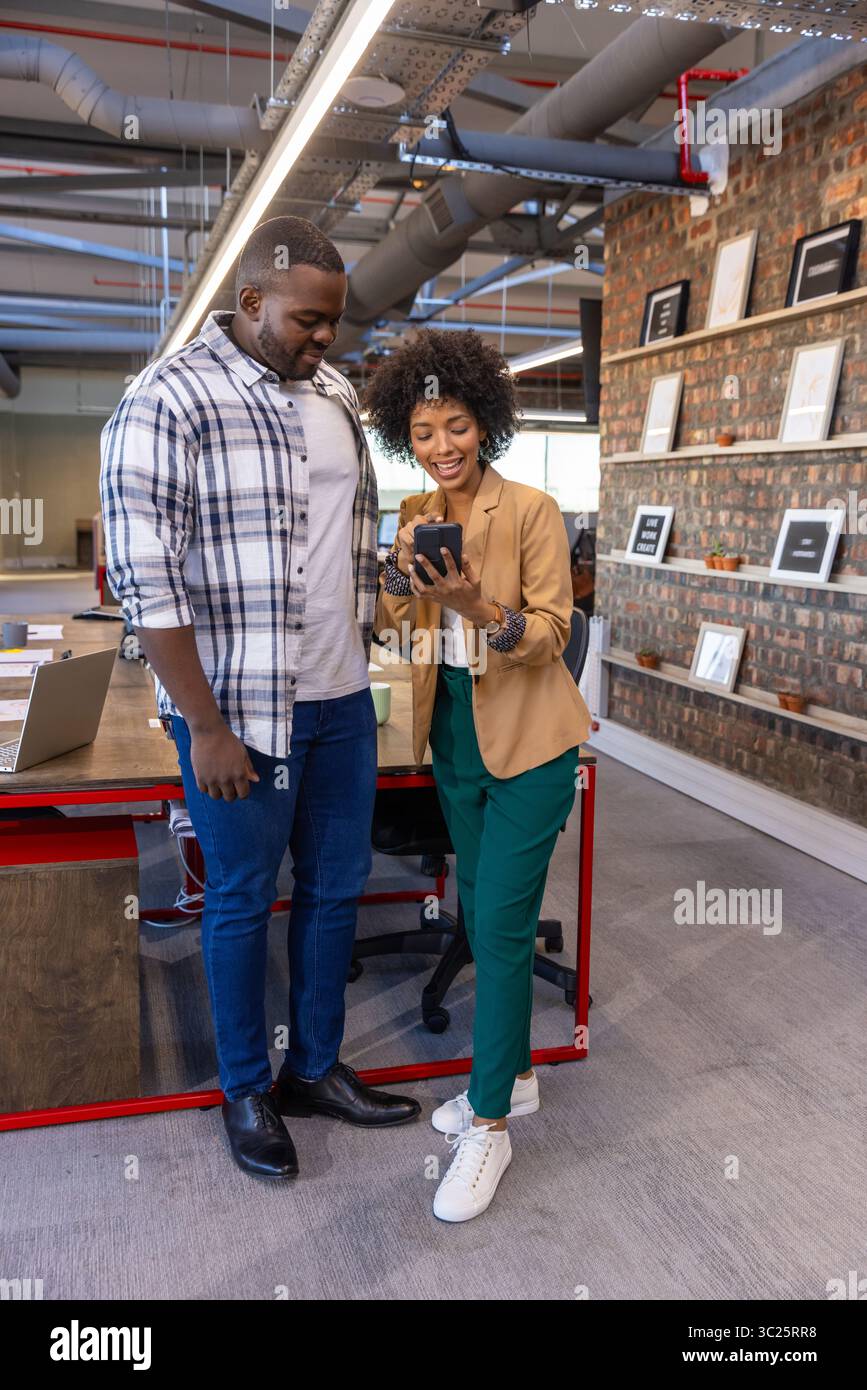 Diverse coworkers standing and reviewing smartphone at wooden desk in office with laptop Stock Photo