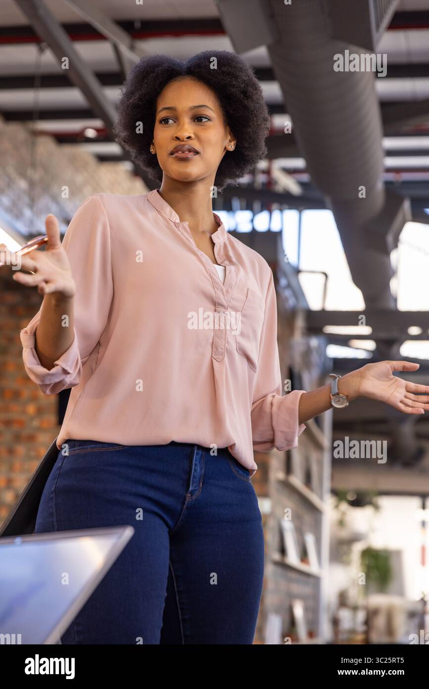 African American businesswoman gesturing while speaking in office with laptop, duct and metal beams Stock Photo