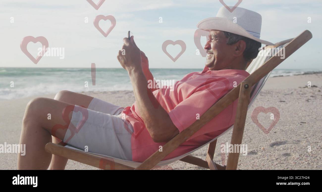Scrolling smartphone senior man wearing straw hat sitting on beach chair, with floating heart icons Stock Photo