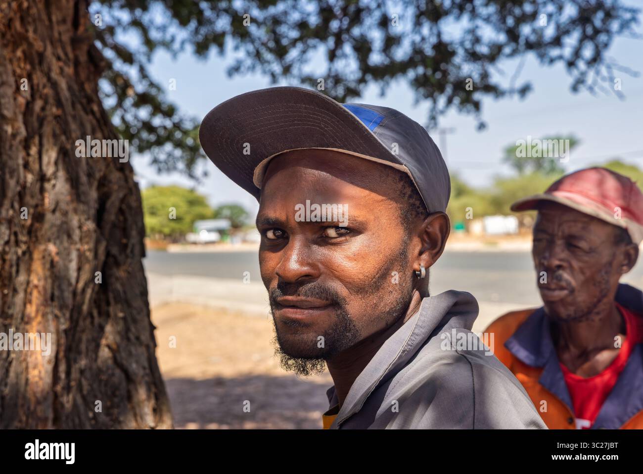 african village, young and old man wearing workwear , houses in the background rural, hard life standing under the shade of a tree Stock Photo