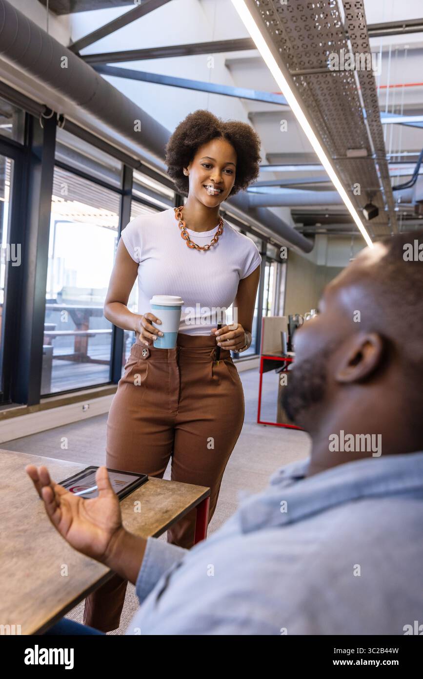 African American coworkers engaging in discussion in coworking space with tablet and coffee cup Stock Photo