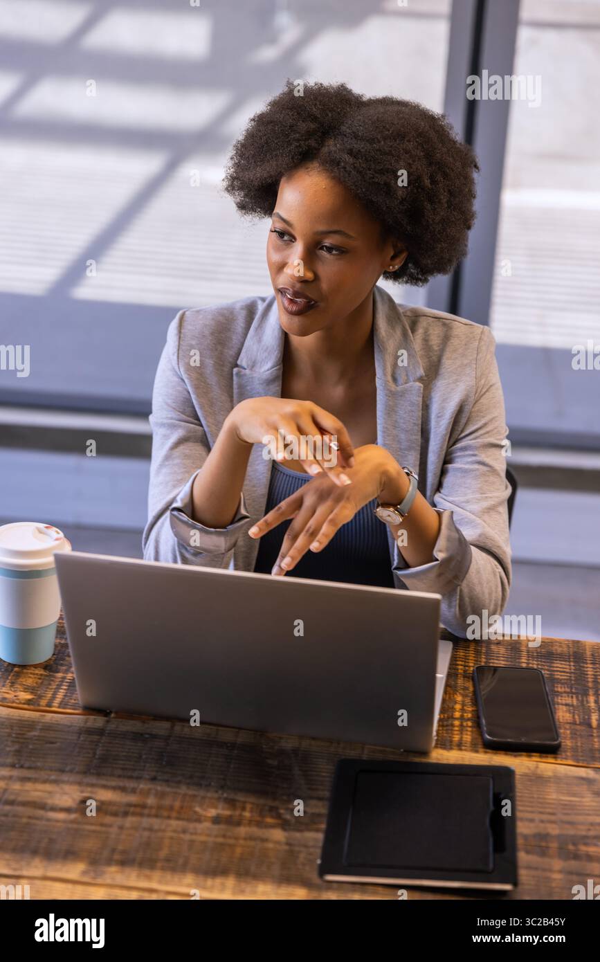 African American woman presenting idea in office with laptop mobile devices coffee cup wristwatch Stock Photo