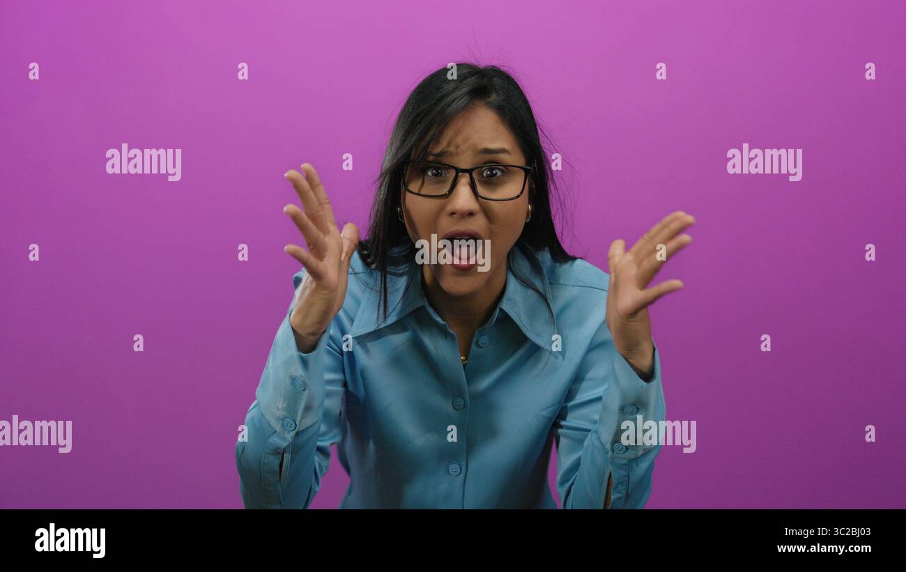 Young hispanic woman in stress holding her head in frustration against an isolated vibrant pink background, expressing overwhelmed emotions. Stock Photo
