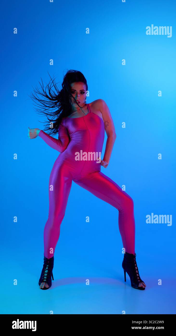 Dancer in pink bodysuit and high heels striking a pose under blue lighting Stock Photo