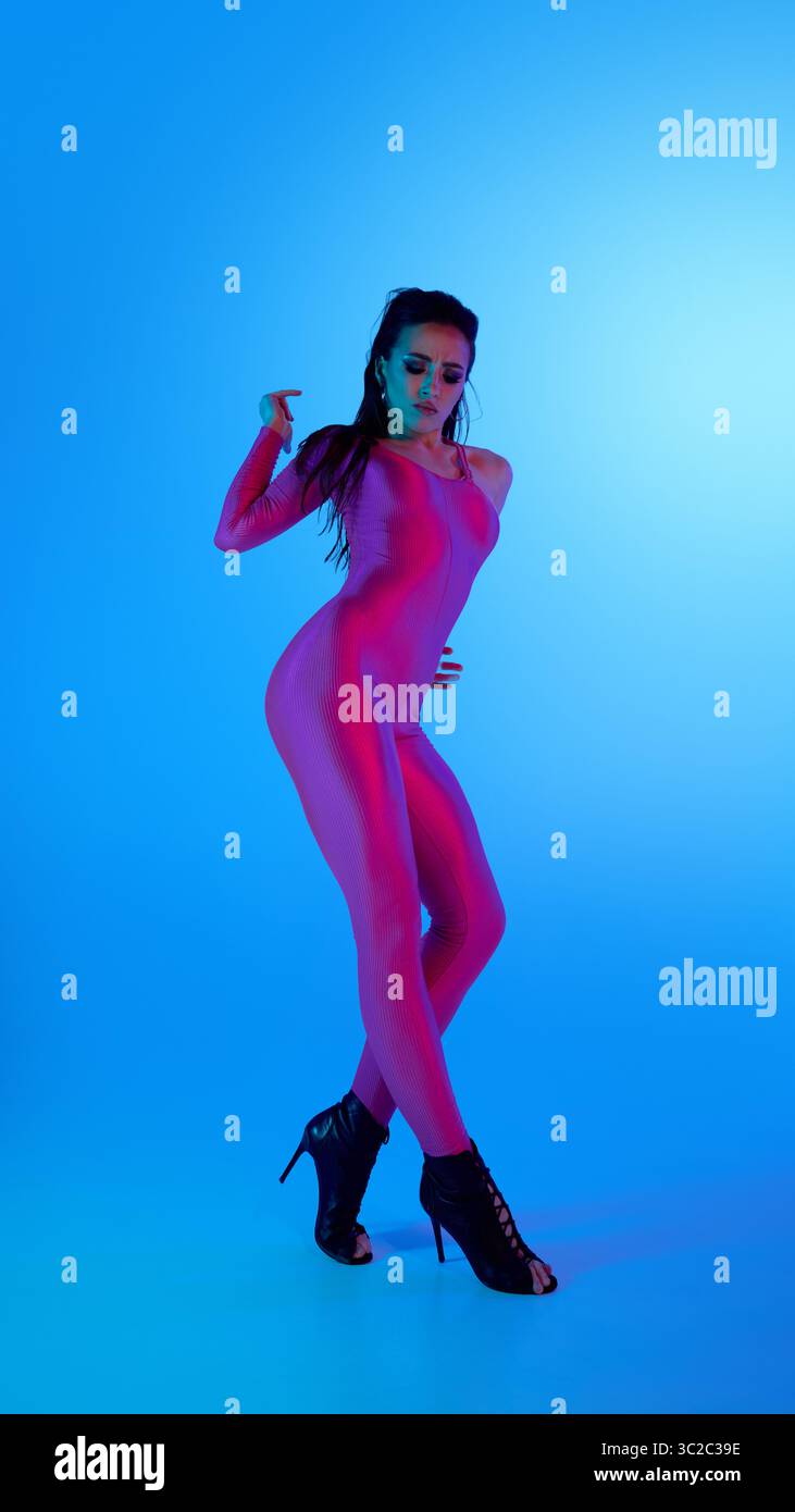 Dancer in vibrant pink outfit poses confidently in high heels with blue background Stock Photo