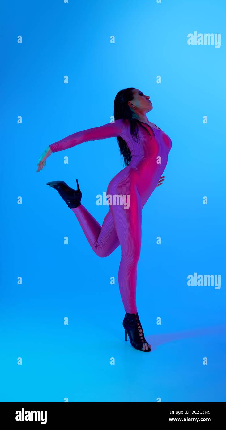 Dancer in vibrant jumpsuit posing elegantly against blue background Stock Photo
