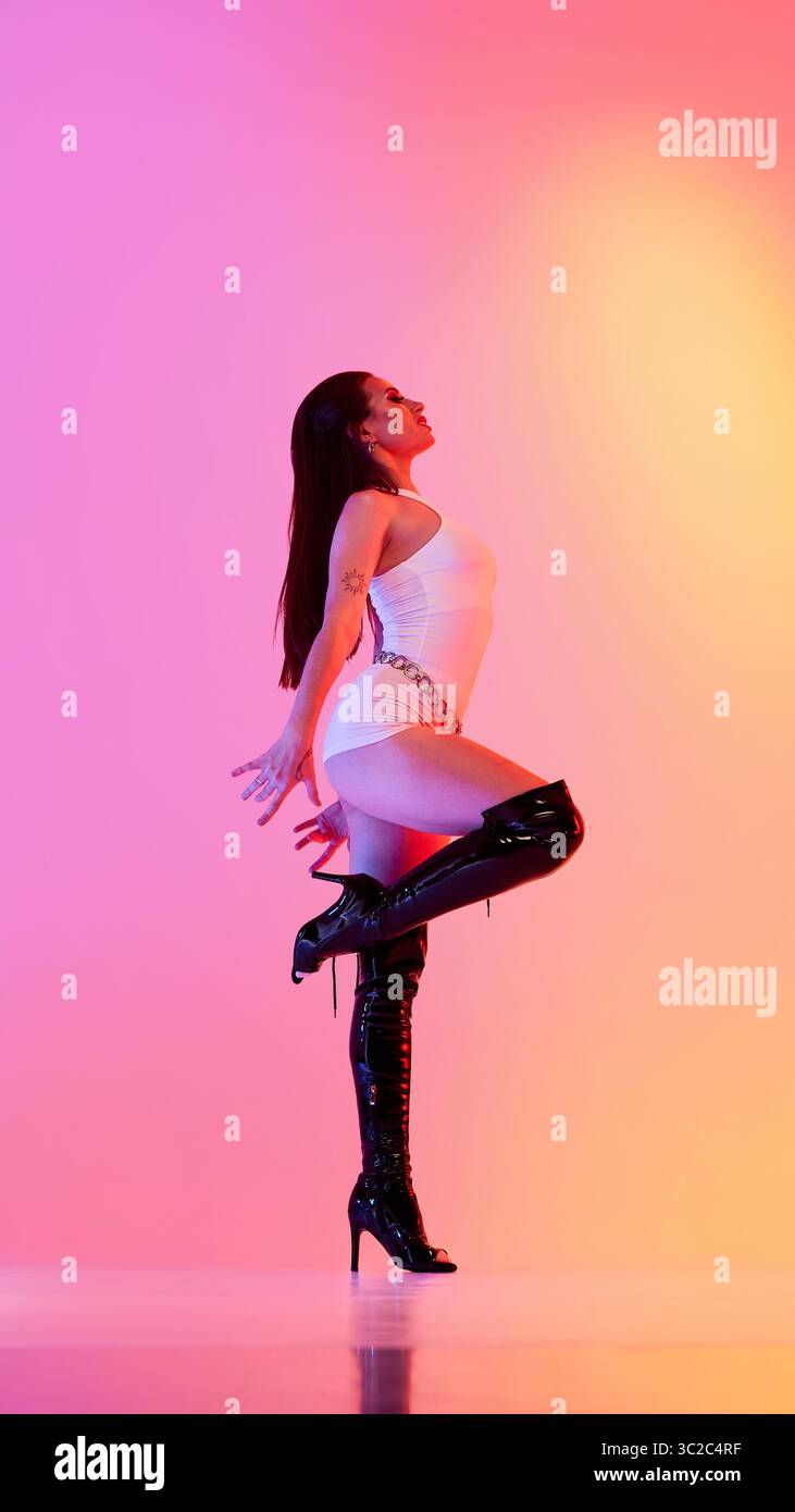Woman performing in high heels against vibrant orange pink backdrop Stock Photo