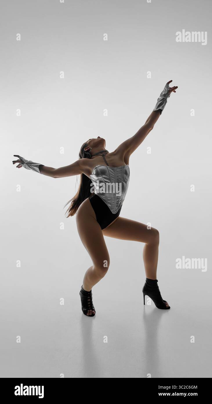 Dancer in silver leotard striking dynamic pose in high heels against white background Stock Photo