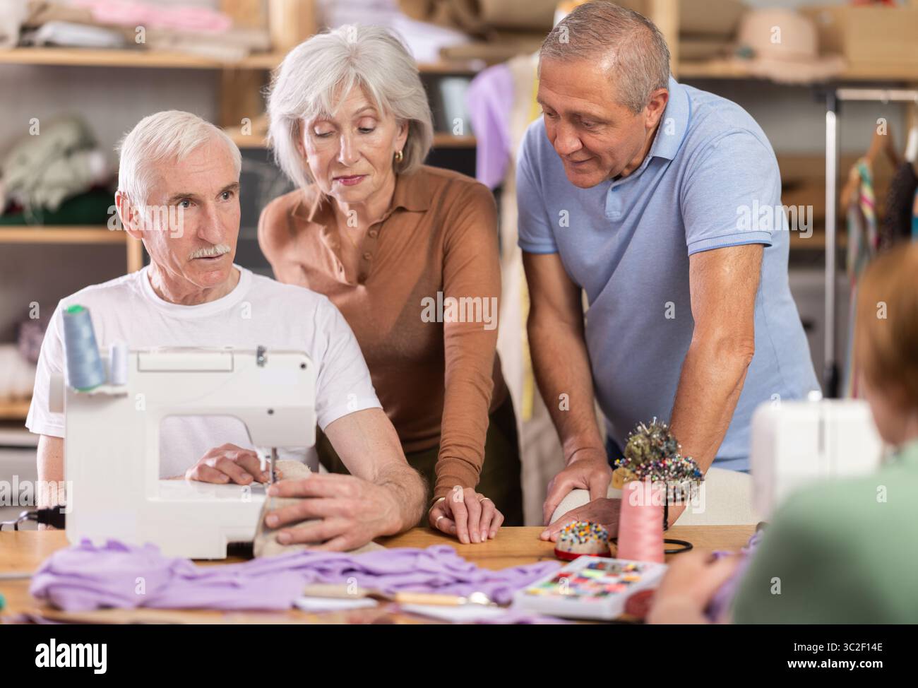 Retired students learning sewing from male instructor in tailoring workshop Stock Photo