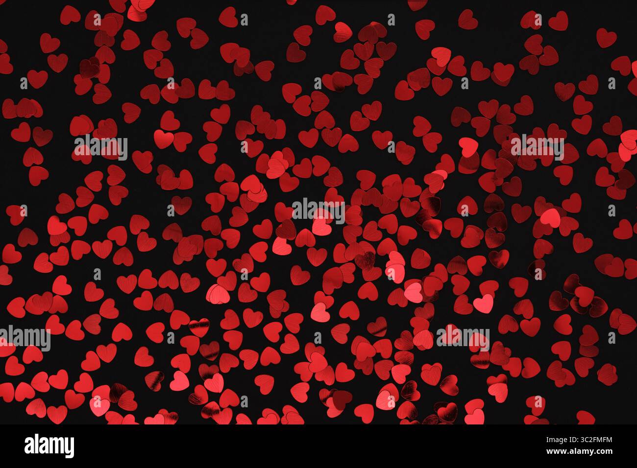 Red glittery heart shaped confetti on a black backdrop. Background pattern. Stock Photo