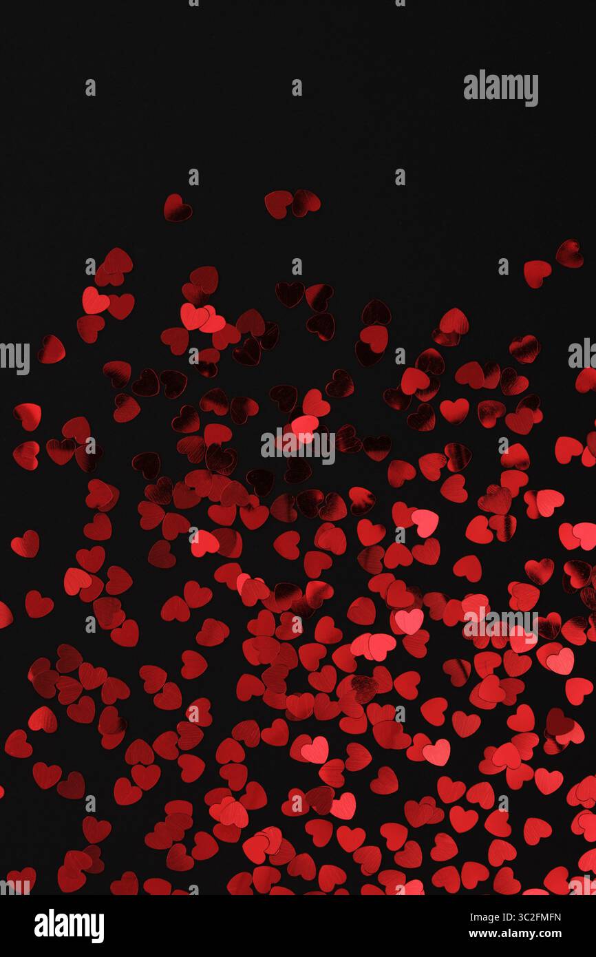 Red glittery heart shaped confetti on a black backdrop. Background pattern. Stock Photo