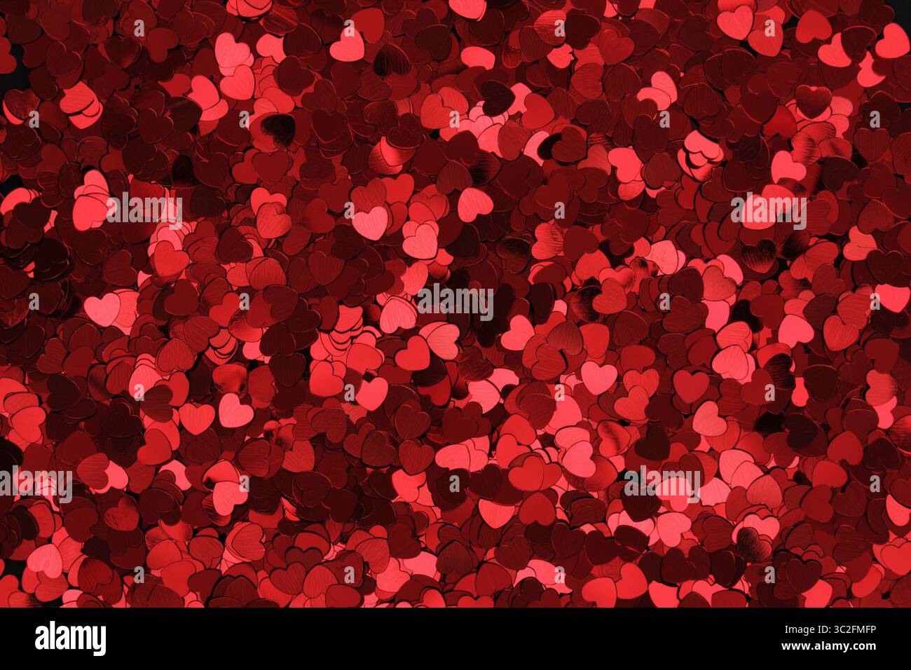 Red glittery heart shaped confetti on a black backdrop. Background pattern. Stock Photo