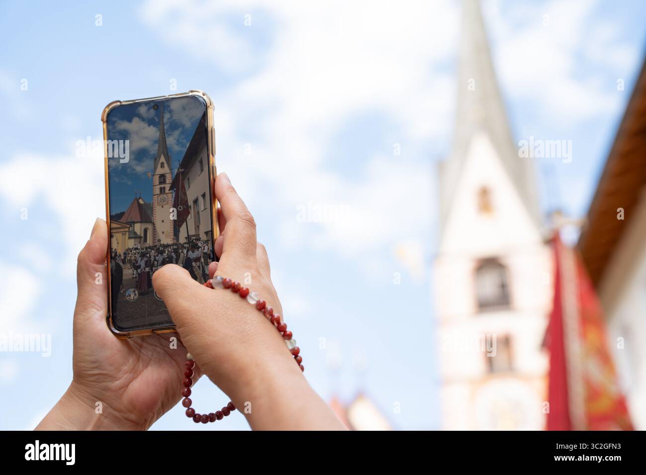 tourist taking a photo of a group of people wearing traditional south tyrolean costumes in front of Santa Cristina church in Val Gardena, Italy Stock Photo