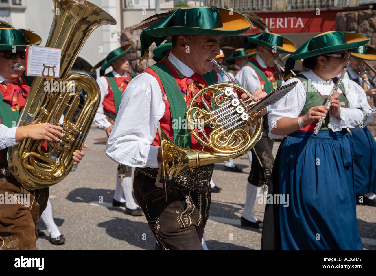 Man playing a French horn in a folk marching band wearing a traditional south tyrolean tracht and lederhosen during a festival in Val Gardena Stock Photo