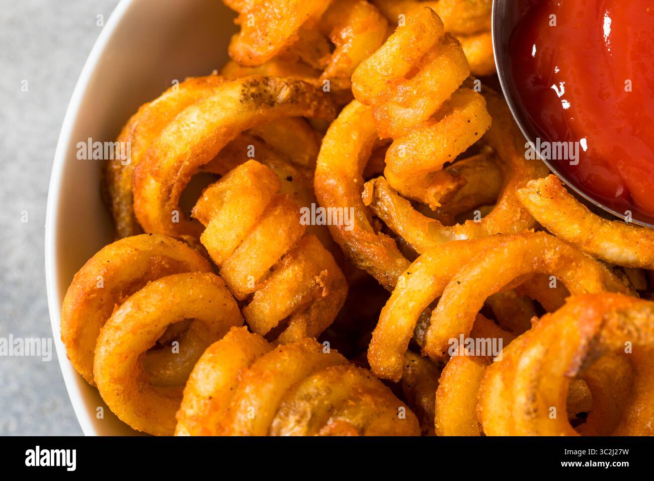 Unhealthy Seasoned Curly French Fries with Ketchup Stock Photo