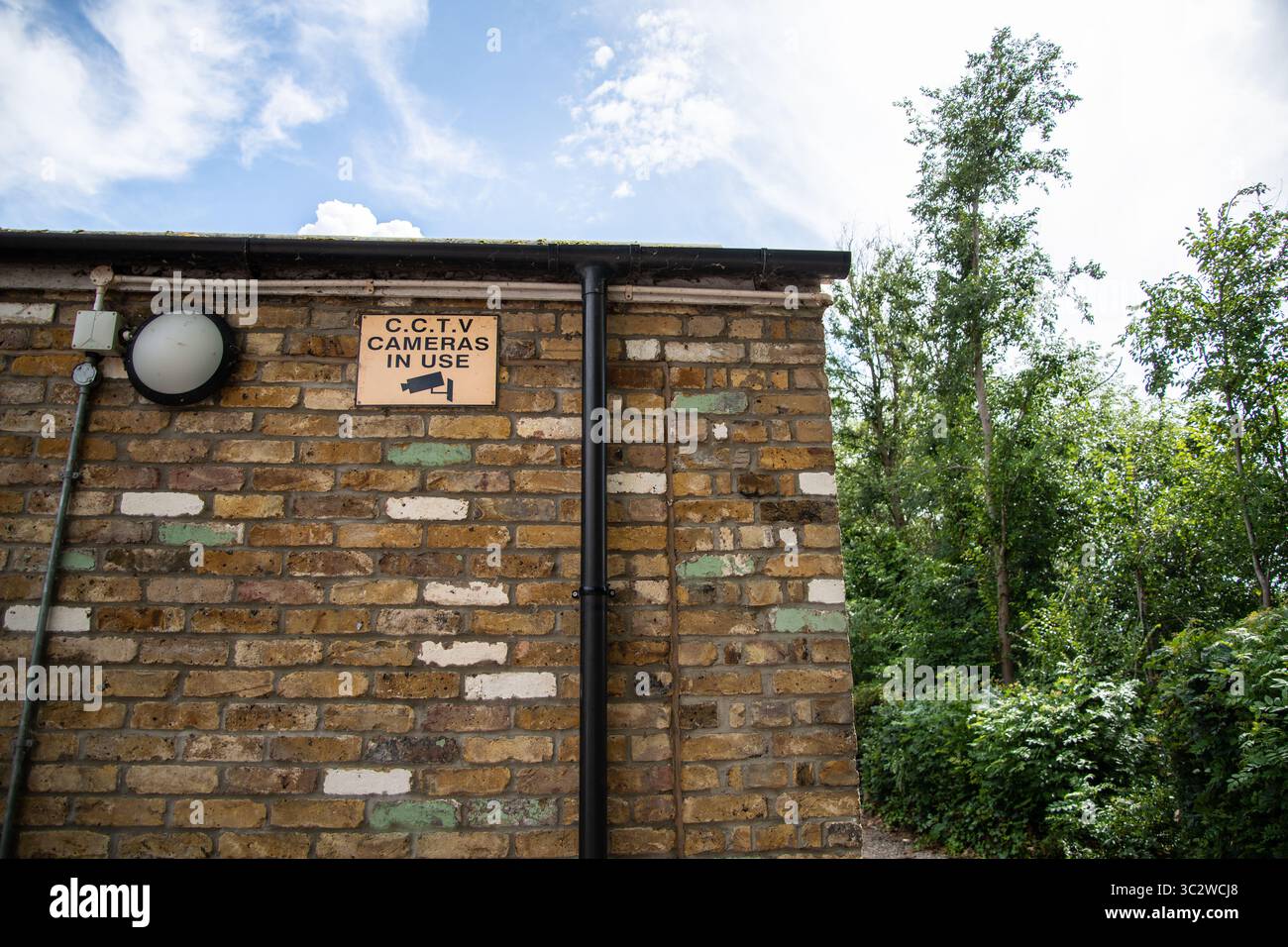 CCTV warning sign with black text on orange background and camera icon, mounted on the side of a brick building, indicating surveillance in operation. Stock Photo