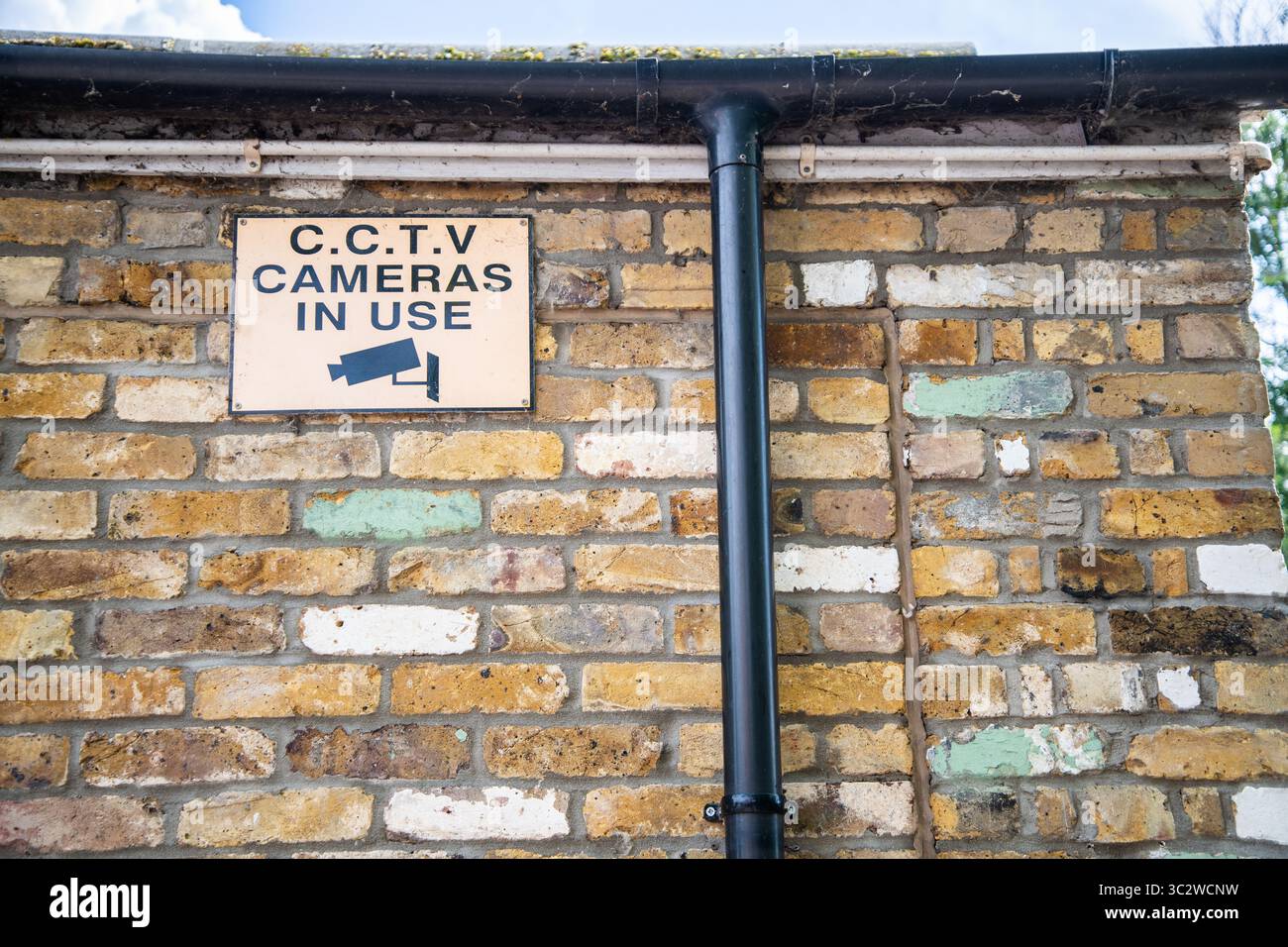 CCTV warning sign with black text on orange background and camera icon, mounted on the side of a brick building, indicating surveillance in operation. Stock Photo