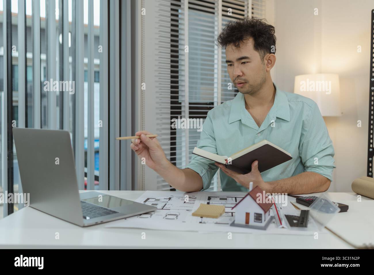 Architect working on house design project using a laptop, holding a ...