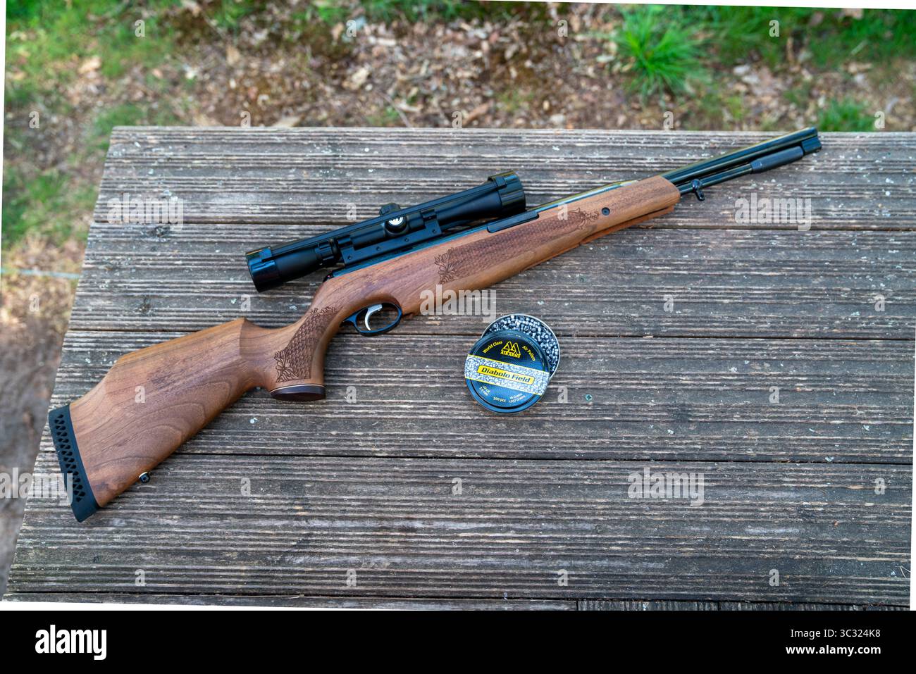 A high-quality air rifle with telescopic sight on a table with a tin of pellets in woodland in southern England Stock Photo