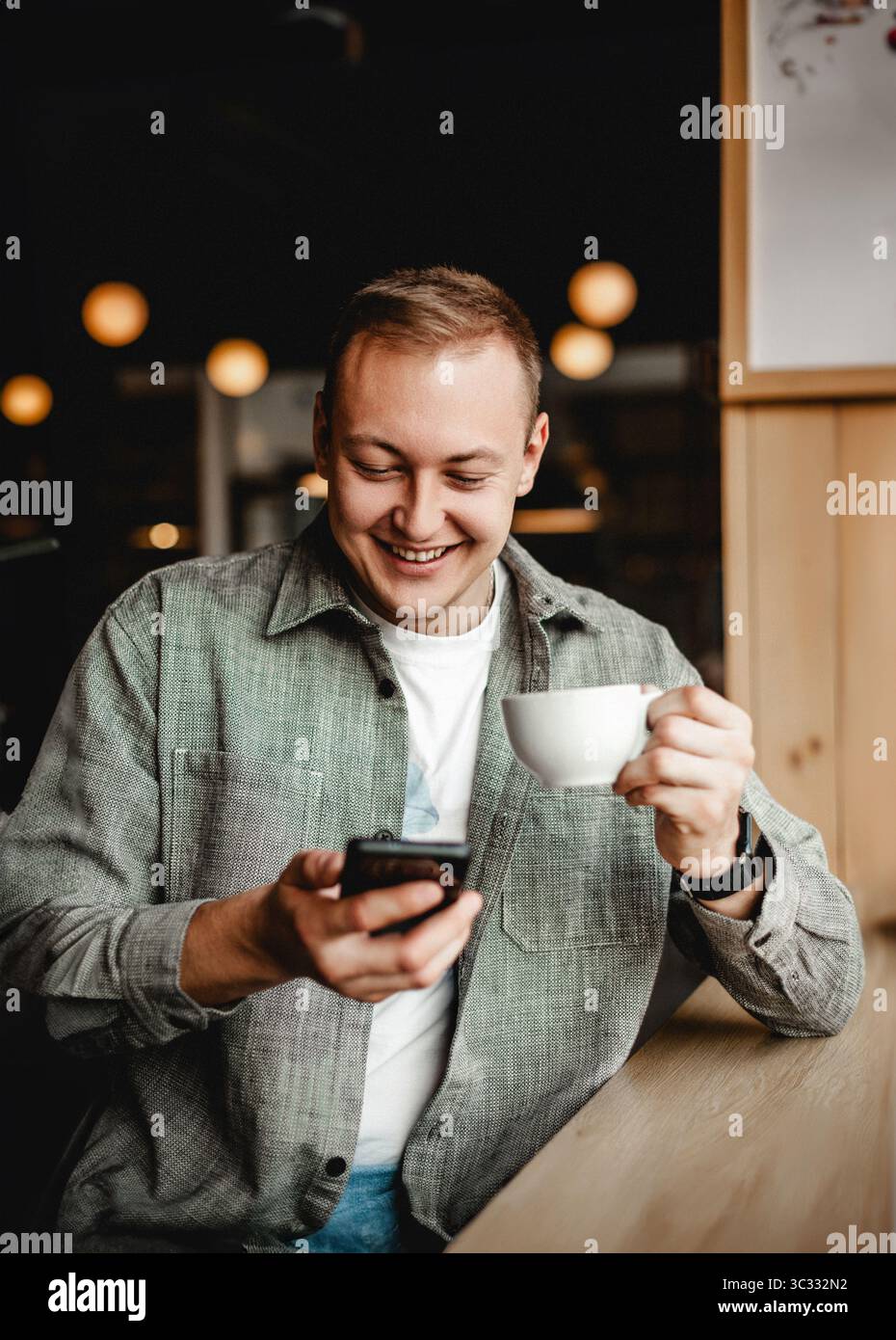 Smiling man using smartphone while drinking coffee Stock Photo