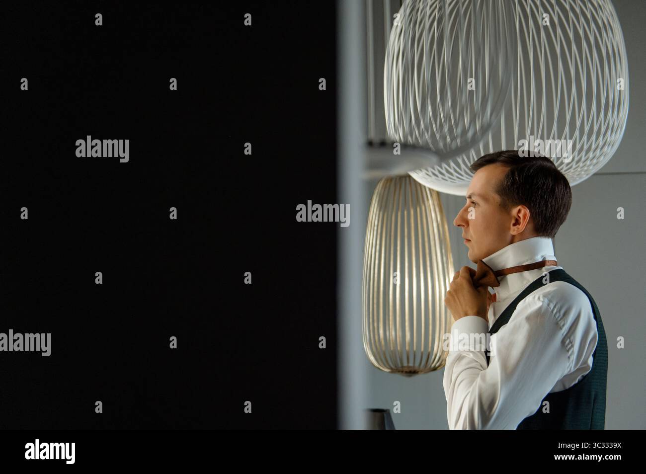 Man adjusting bowtie in modern interior with stylish lighting Stock Photo