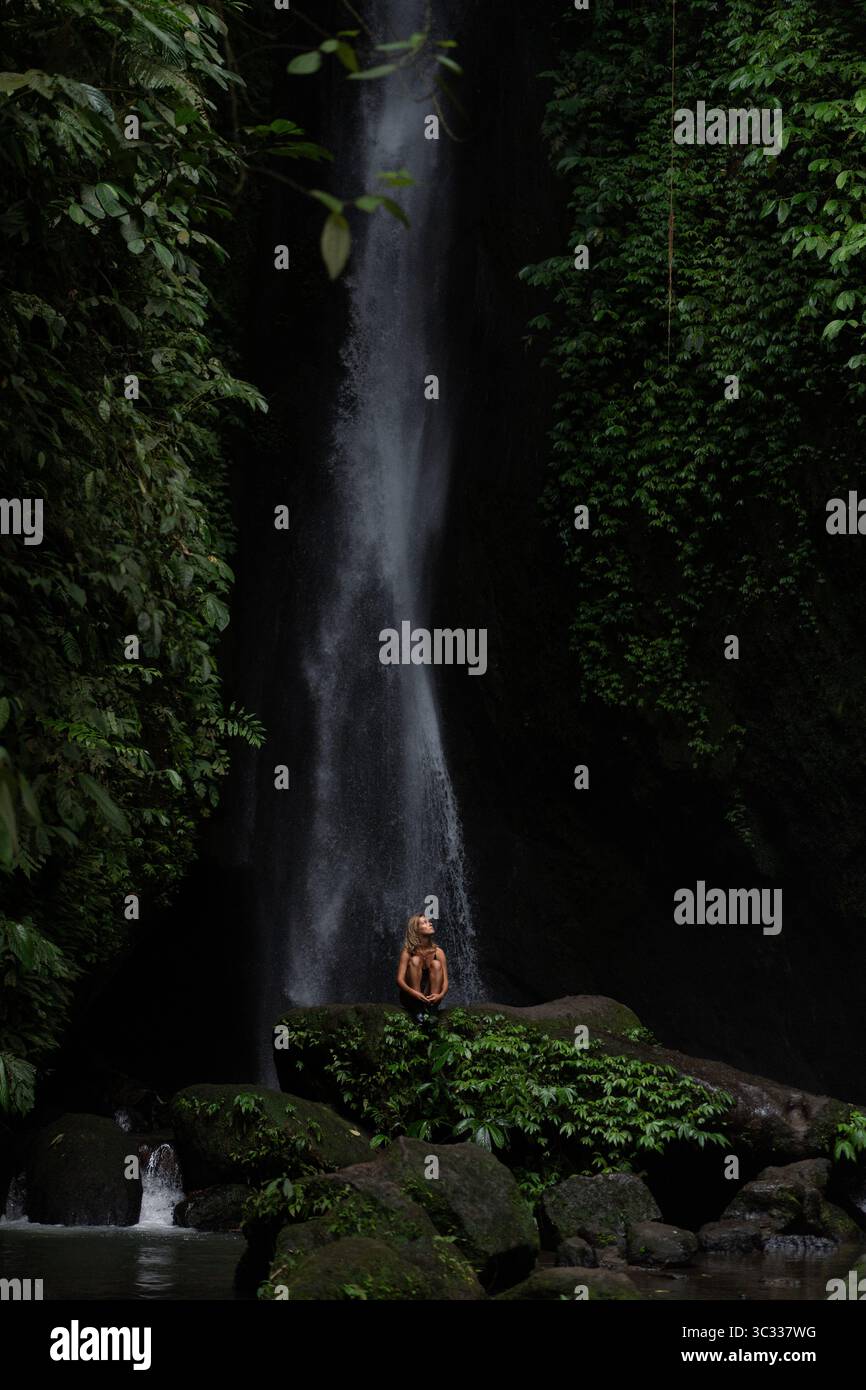 Woman meditating on rocks by a waterfall in the jungle of Bali Stock ...