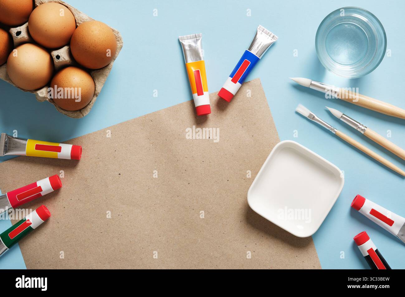 Easter egg decoration and creative preparation. A cardboard sheet on a blue background with brown eggs, brushes, and paint tubes. Stock Photo