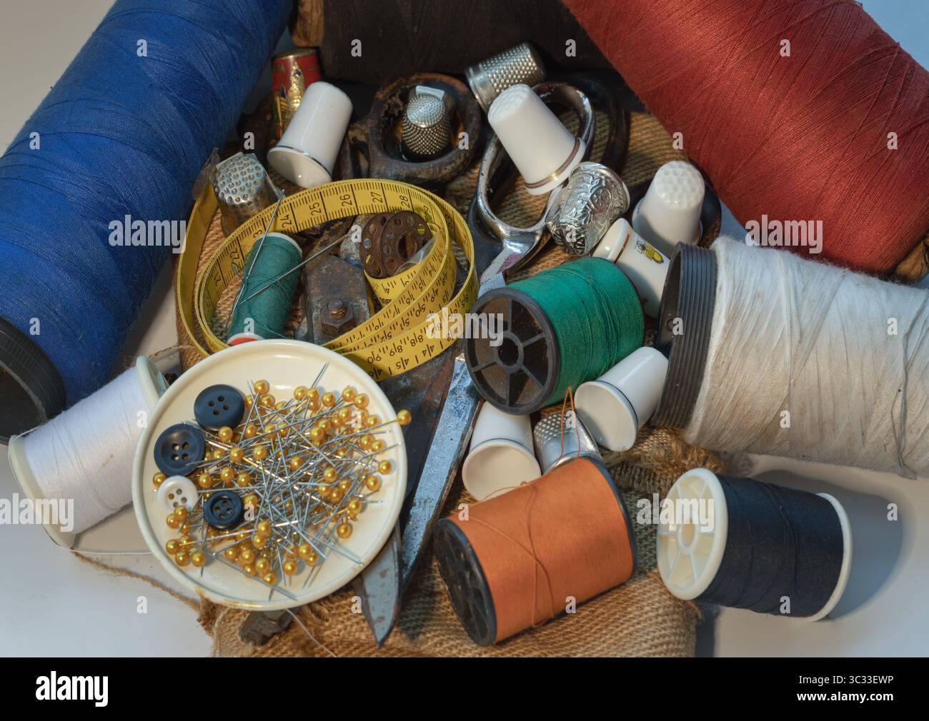 Sewing needles stuck in a green miniature spools thread Steel scissors, Spools of thread of various colour, Thimbles and Measuring tape including Pins Stock Photo