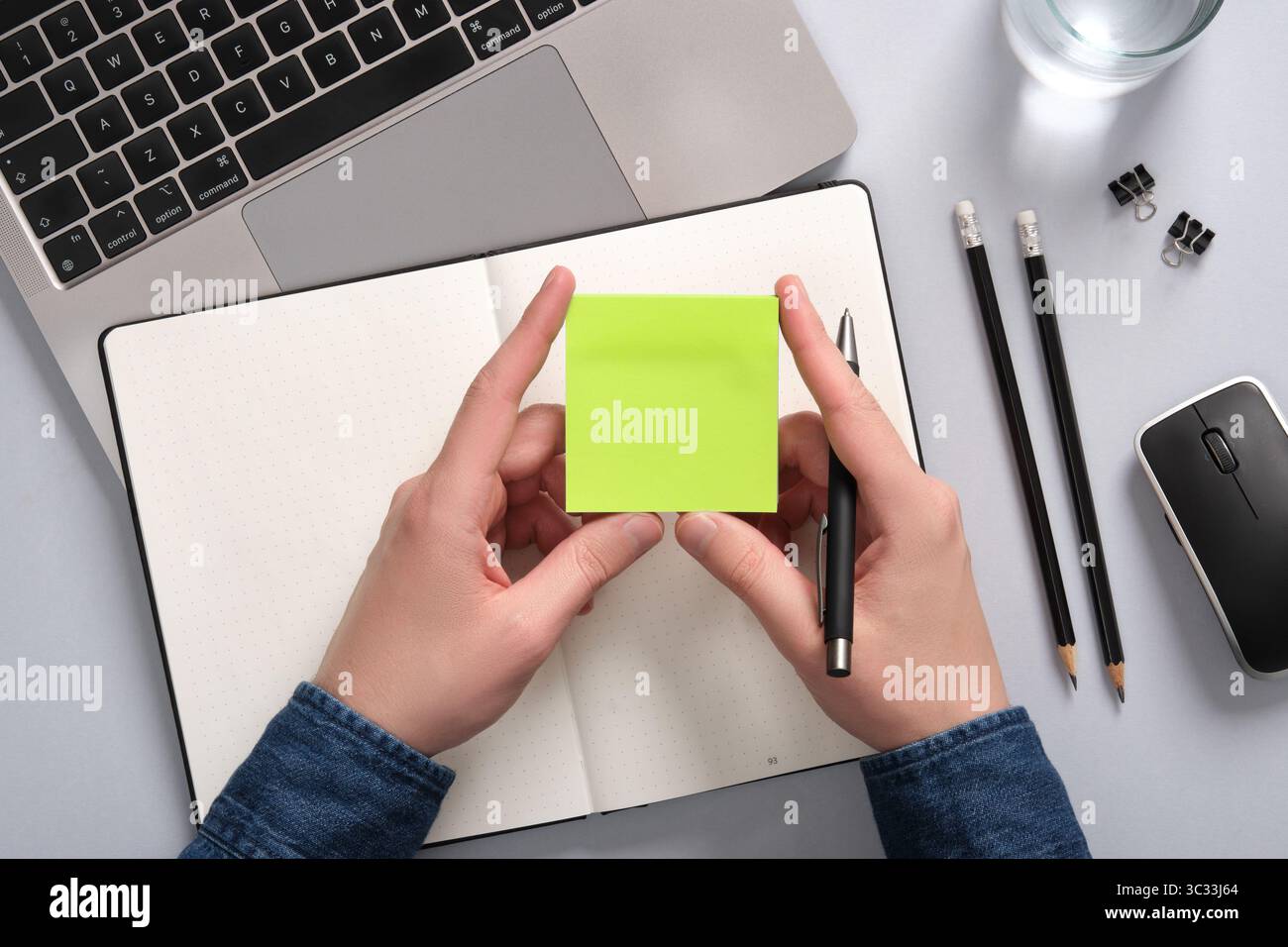 Hands holding a blank sticky note in green over an open notepad on a table. A place for your text Stock Photo