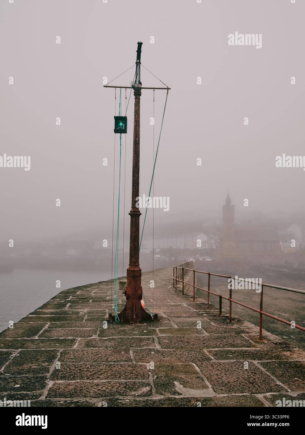 The harbour wall and green port navigation light on a foggy misty day in Porthleven a fishing port in Cornwall, England. UK Stock Photo