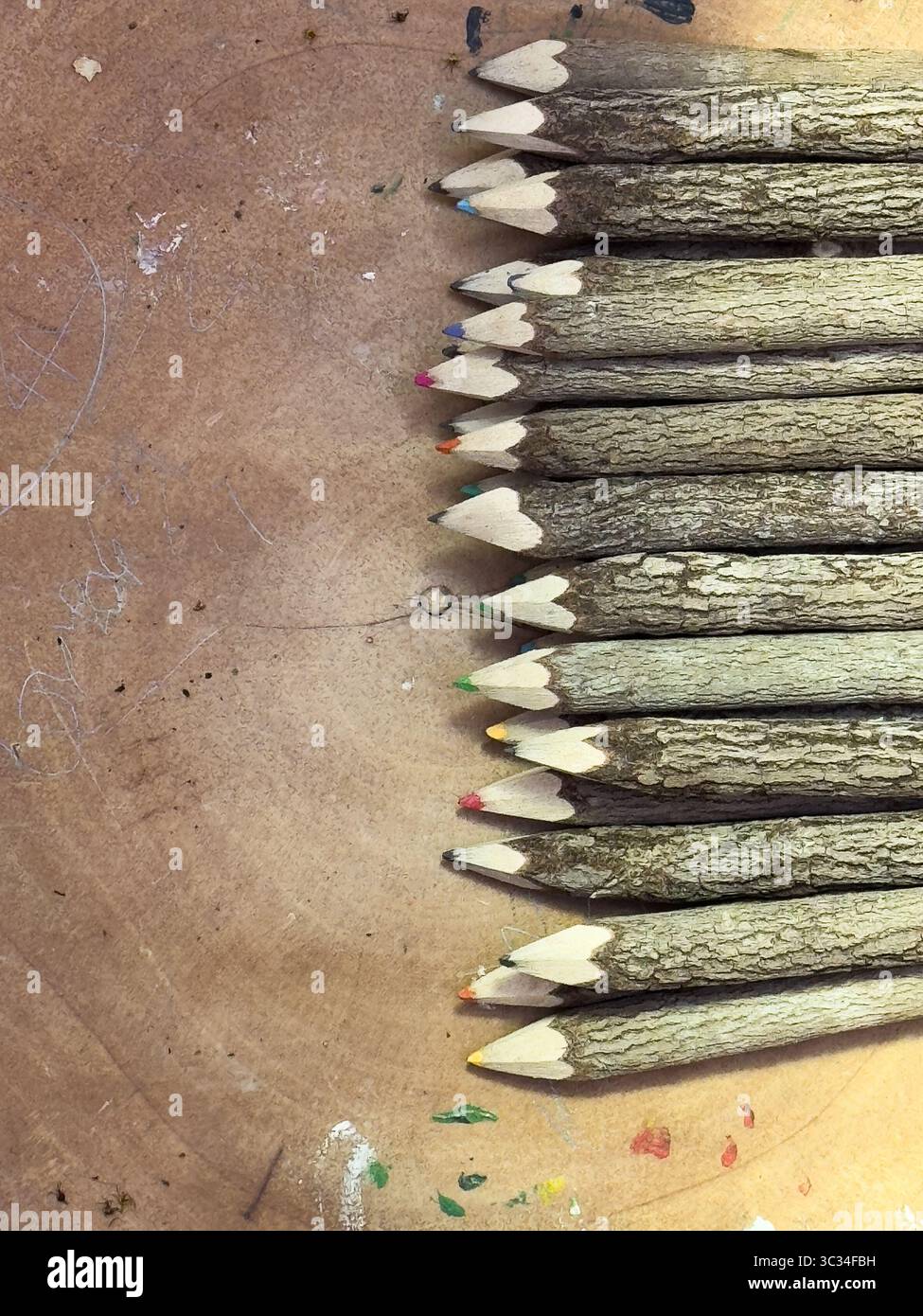 Wooden coloured pencils in a row on a rustic wooden surface. Stock Photo
