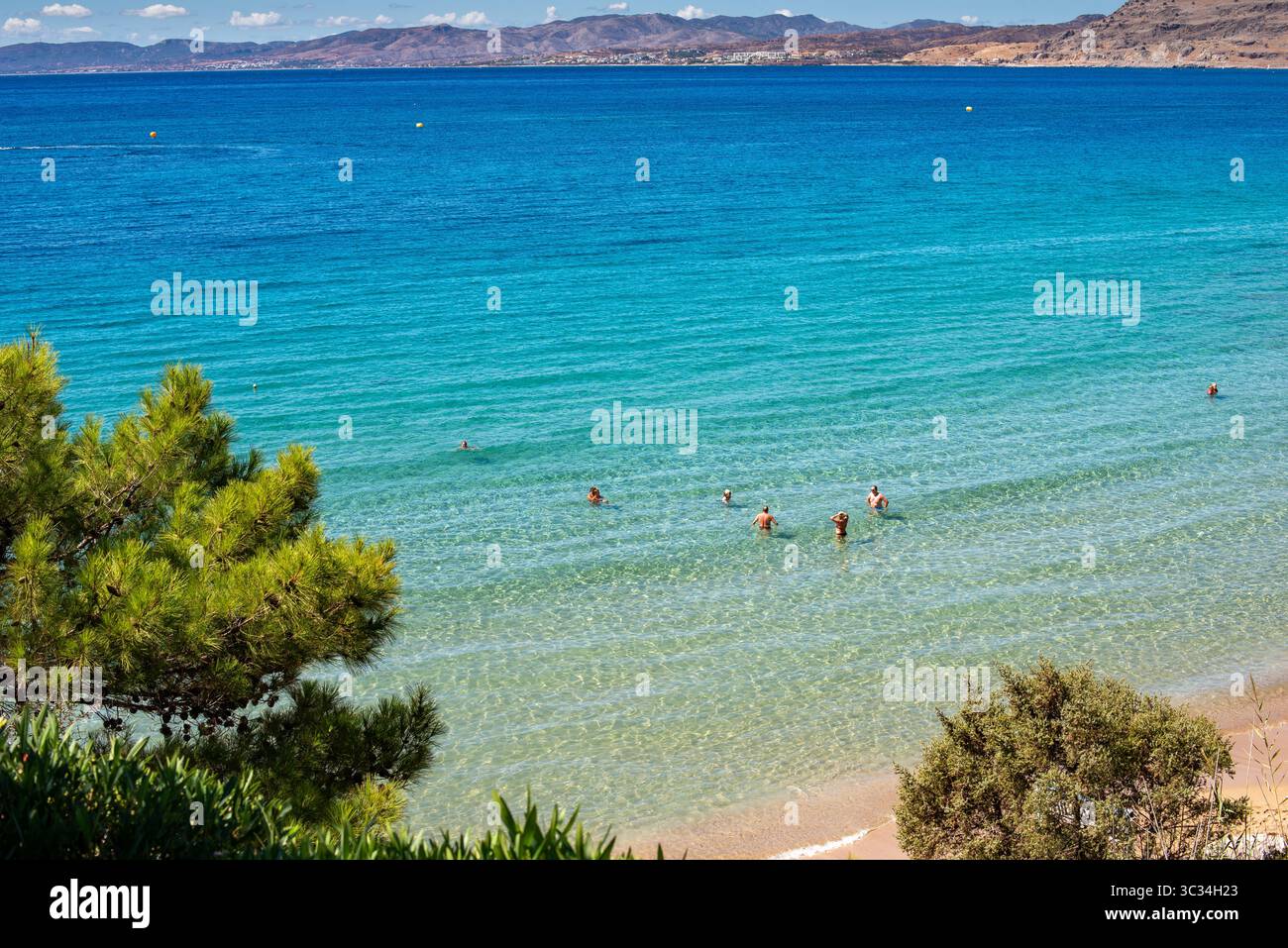 Paralia Pefkos Beach with Swimmers and View Across the Bay to Lardos, Rhodes, Greece (landscape orientation) Stock Photo