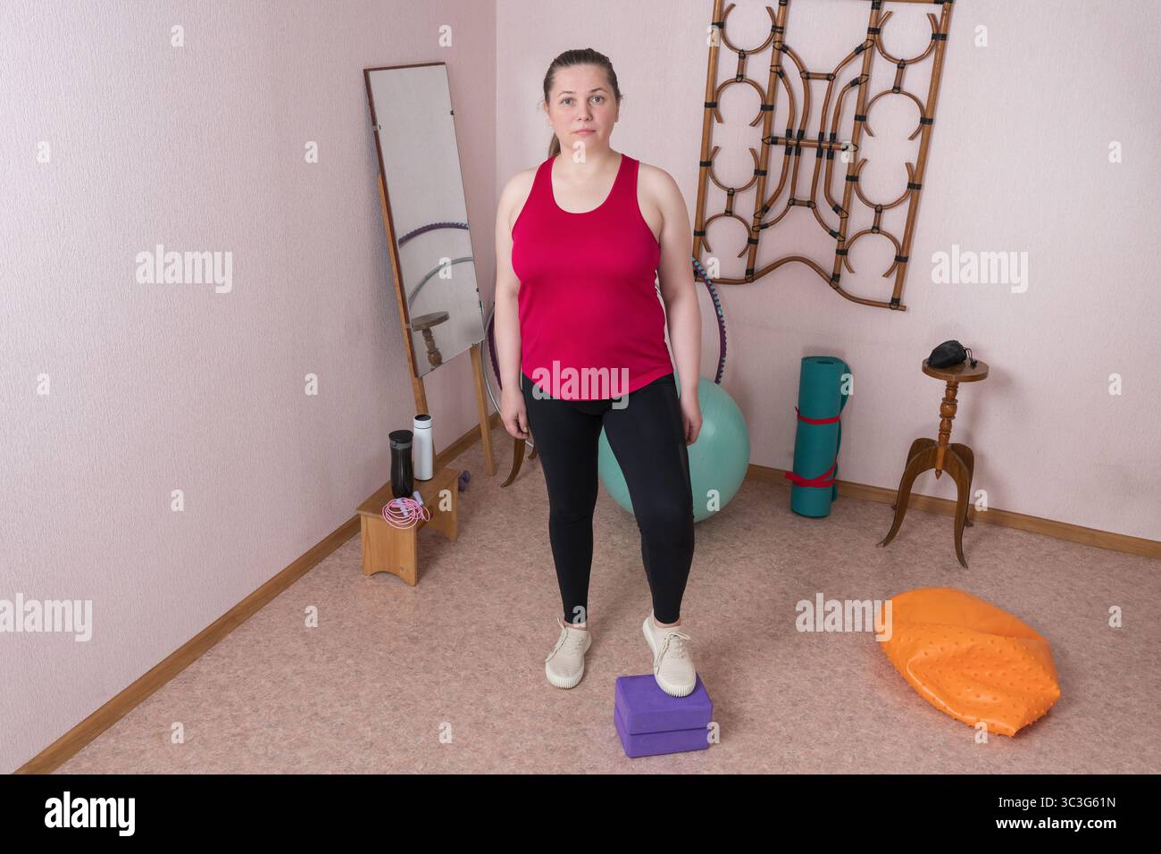 Full length view of 44 year old woman is standing during pilates workout at her indoor home exercise area. Woman is Generation X dressed in sportswear Stock Photo