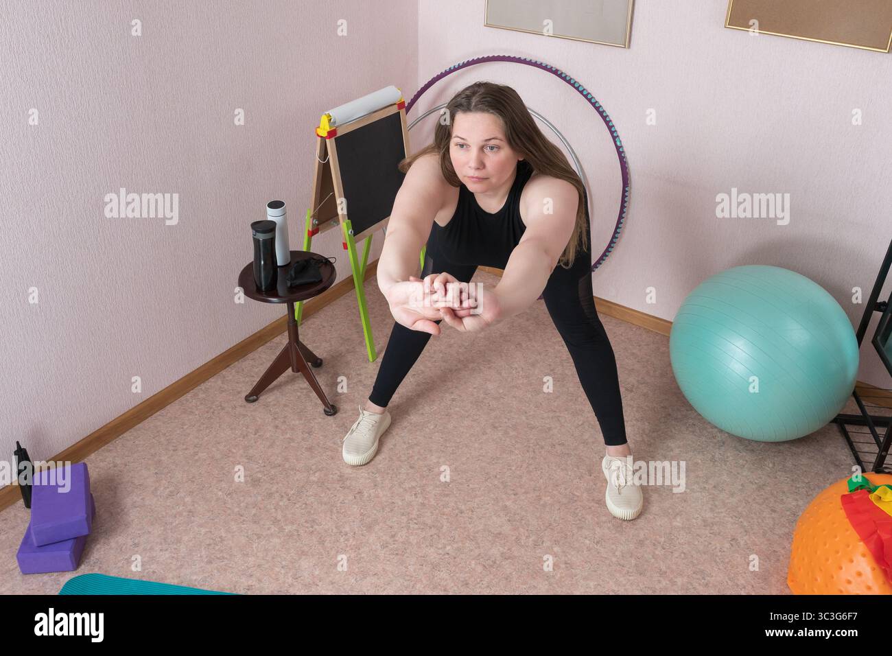 Mature woman is performing forward bend during domestic fitness regimen. Full length view of adult fitness woman of Caucasian ethnicity attired in bla Stock Photo