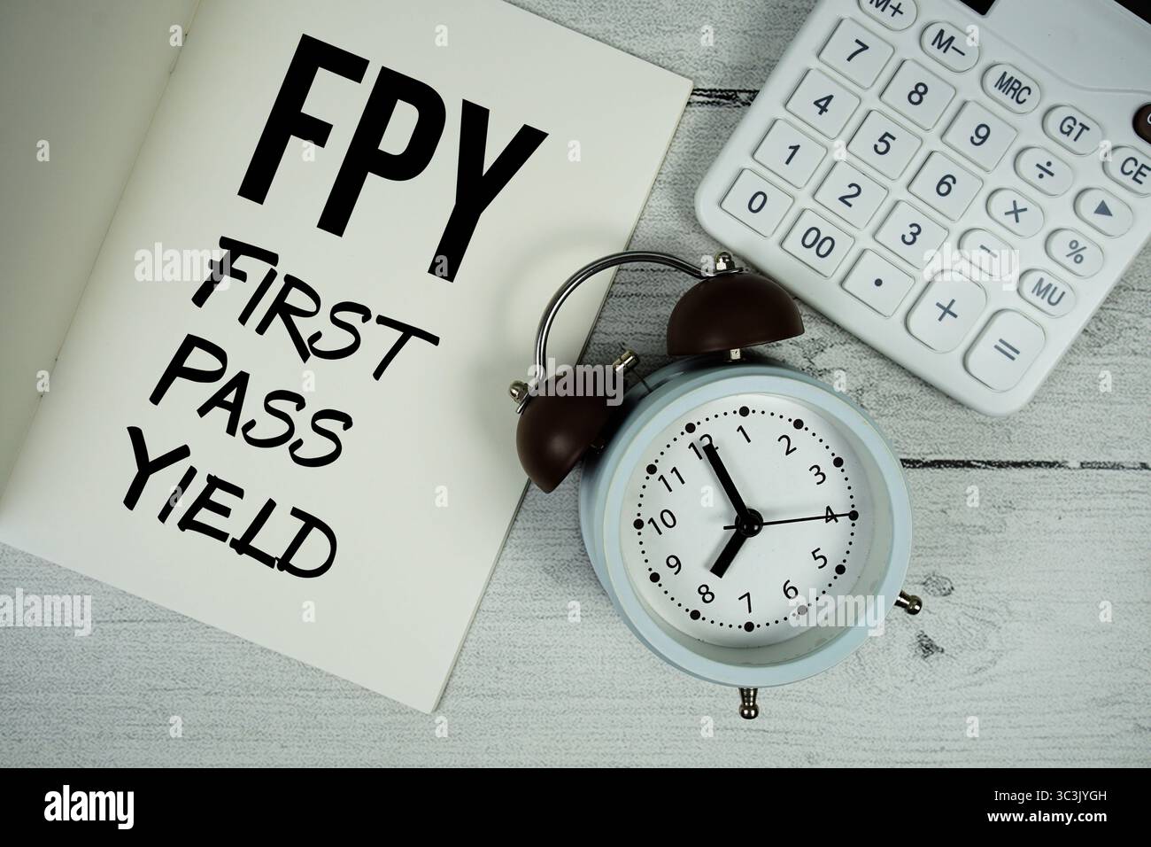 FPY First Pass Yield text on paper notebook page with alarm clock and calculator on wooden background Stock Photo