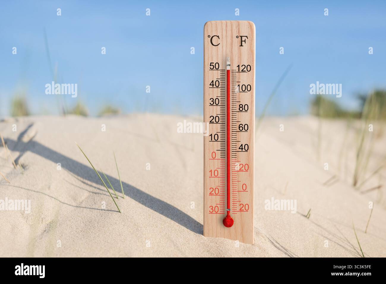 Wooden celsius and fahrenheit scale thermometer in the sand. Ambient temperature plus 50 degrees. Hot summer day Stock Photo
