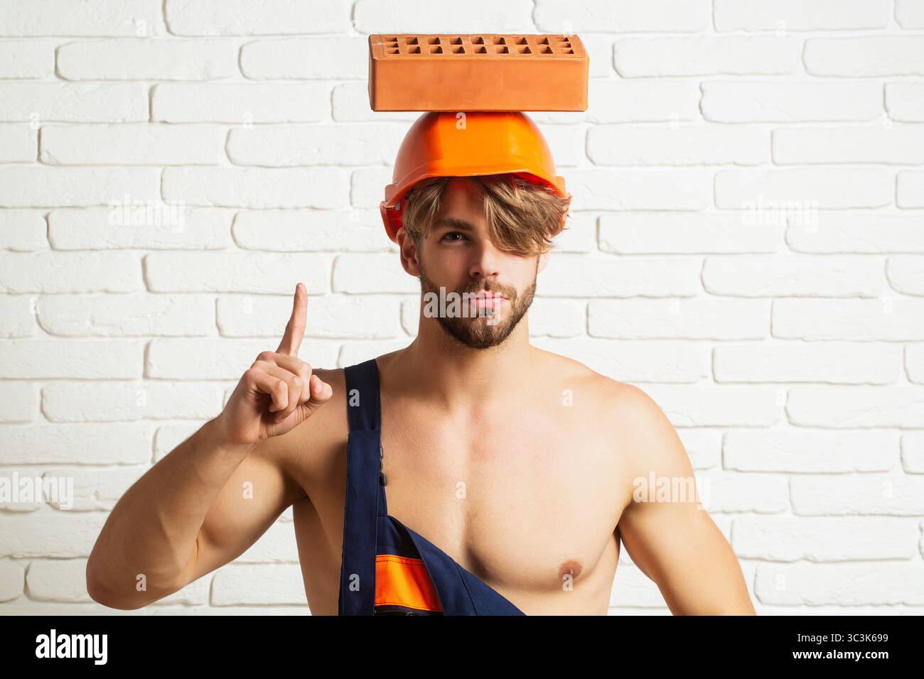Builder with bricks, funny sale on construction site. Funny builder man with helmet doing brickwork. Builder posing with bricks blocks. Bricklayer Stock Photo