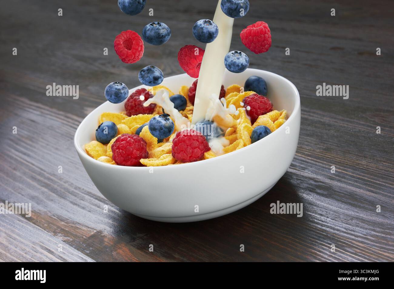 Falling corn flakes with fresh berries and pouring milk on wooden background Stock Photo