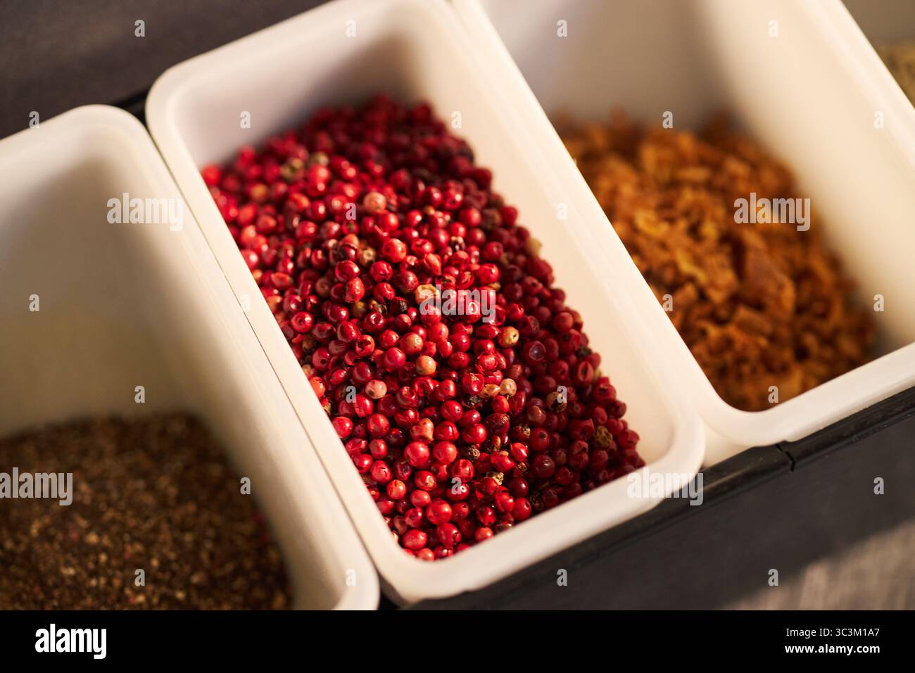 Closeup showing containers filled with red peppercorns, dried herbs, and spices arranged in row, emphasizing variety of culinary ingredients used for cooking and seasoning food Stock Photo