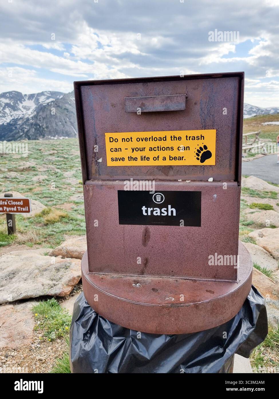 Metal waste bin / trash can with text 'Do not overload trash can - your actions can save the life of a bear'; NP tundra & mountains in background Stock Photo