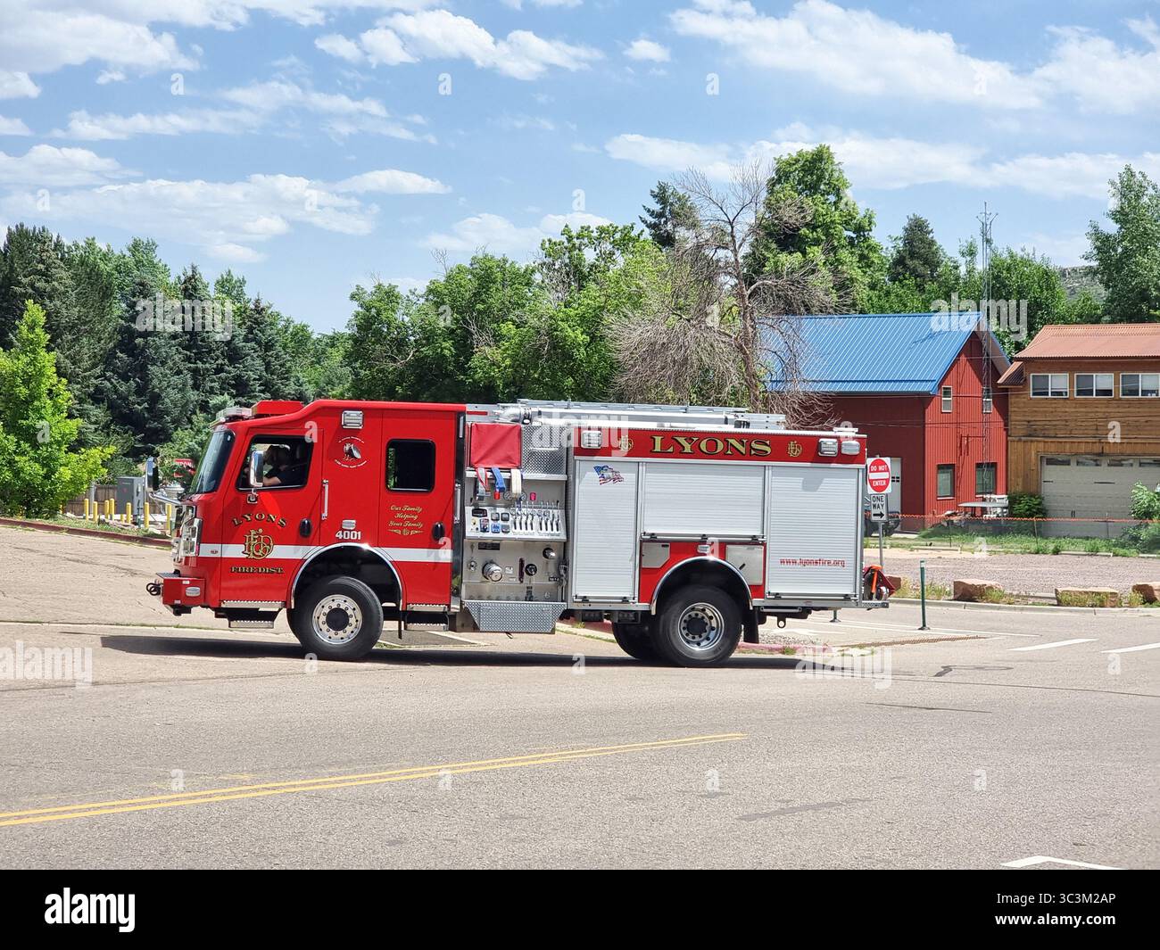 Shiny red fire truck of the fire department / fire brigade of Lyons CO, Colorado, U.S.A.; trees / forest & barns in the background - Smartphone Captured Stock Image