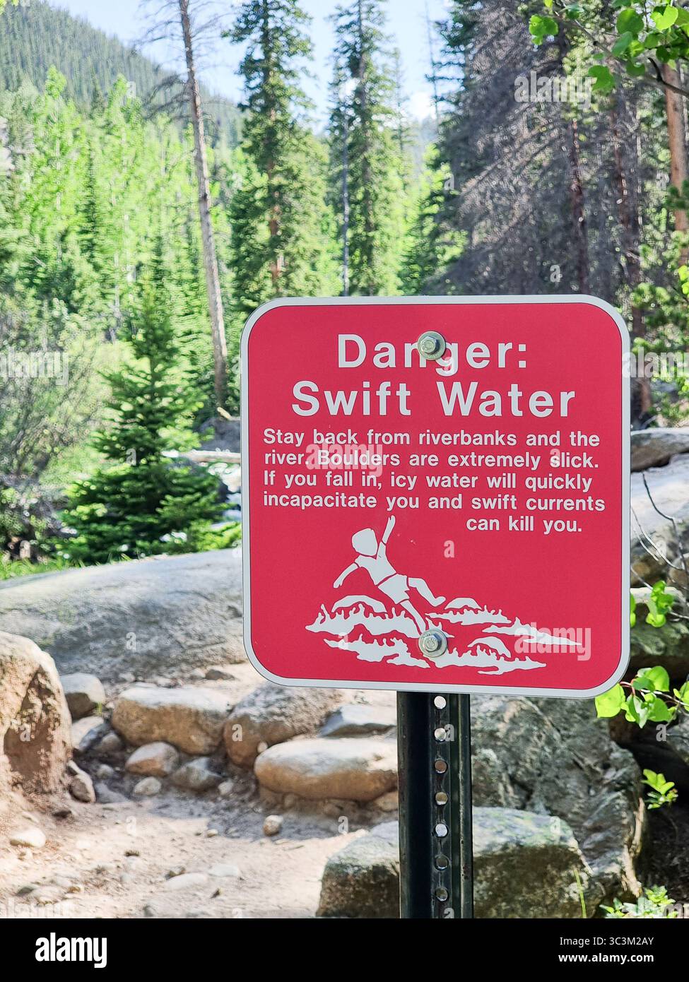 Warning sign with icon and text 'Danger: swift water' near a water stream with slippery rocks in a forest (Rocky Mountain National Park) - Smartphone Captured Stock Image